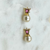 Pair of pearl earrings with gold crowns and pink centers on a white marble surface.